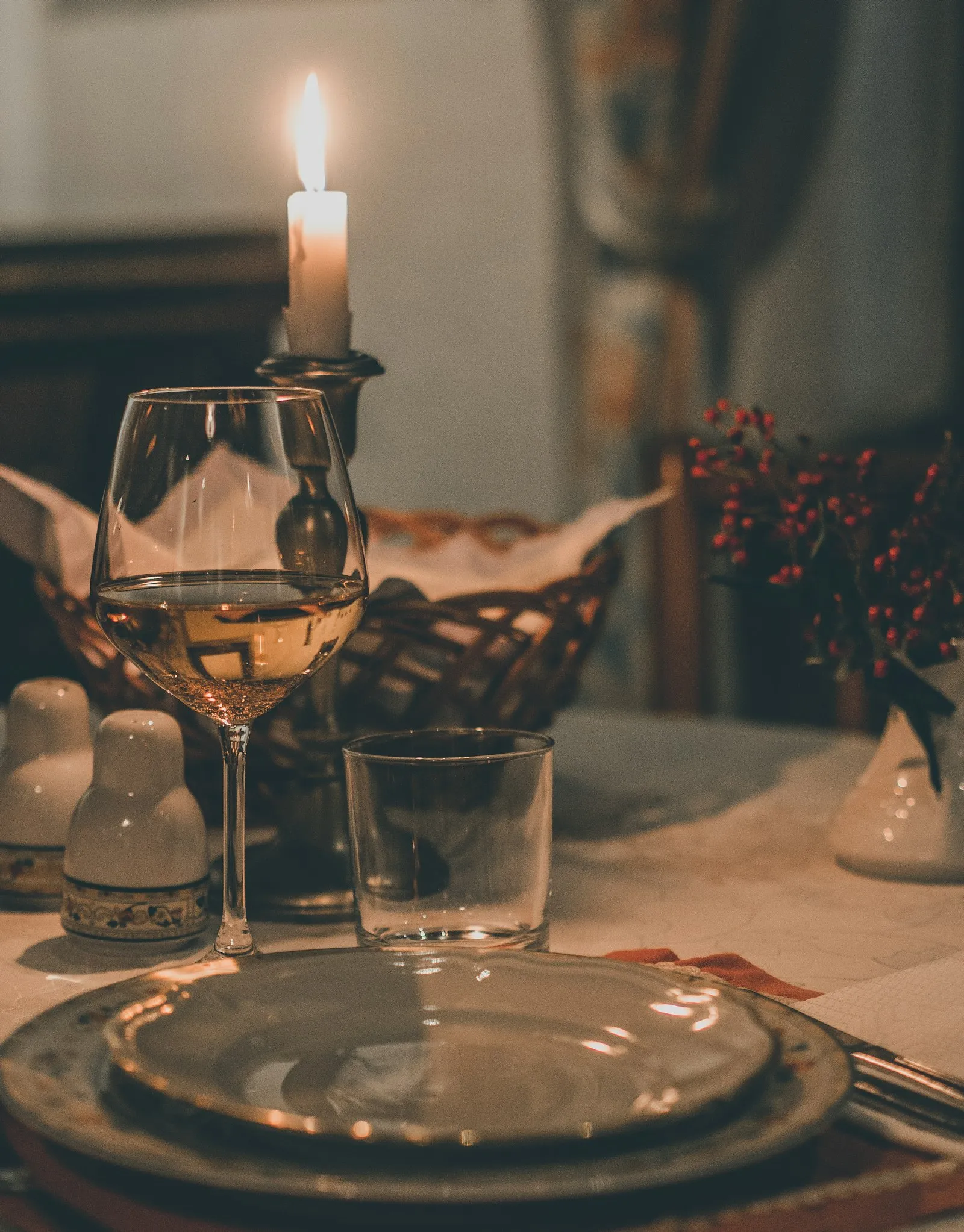 Mesa posta à luz de velas, com taça de vinho e louça elegante.